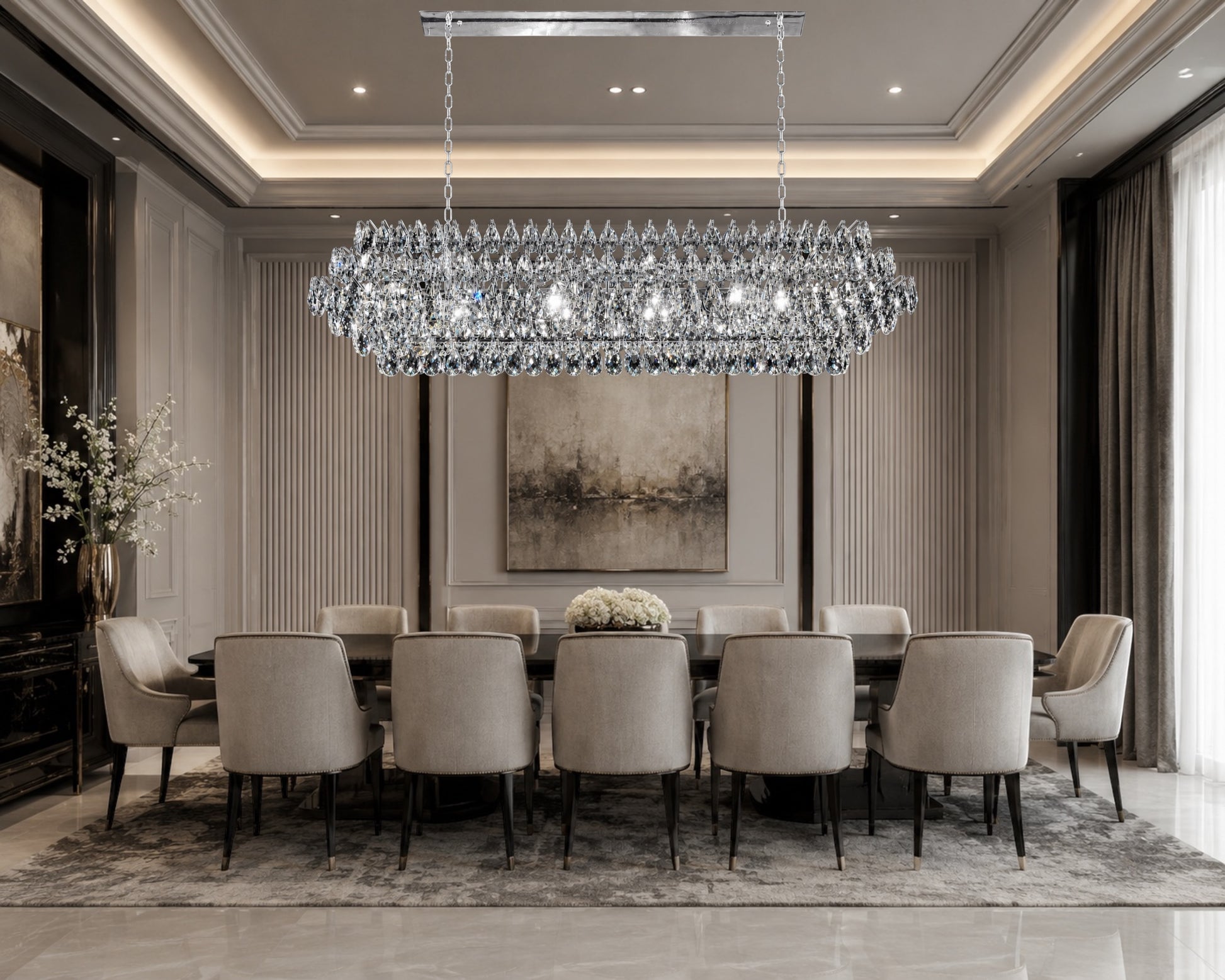 A luxurious linear crystal chandelier with a chrome frame illuminated over a large, elegant dining table with beige chairs in a modern, high-ceiling luxury dining room with large windows.