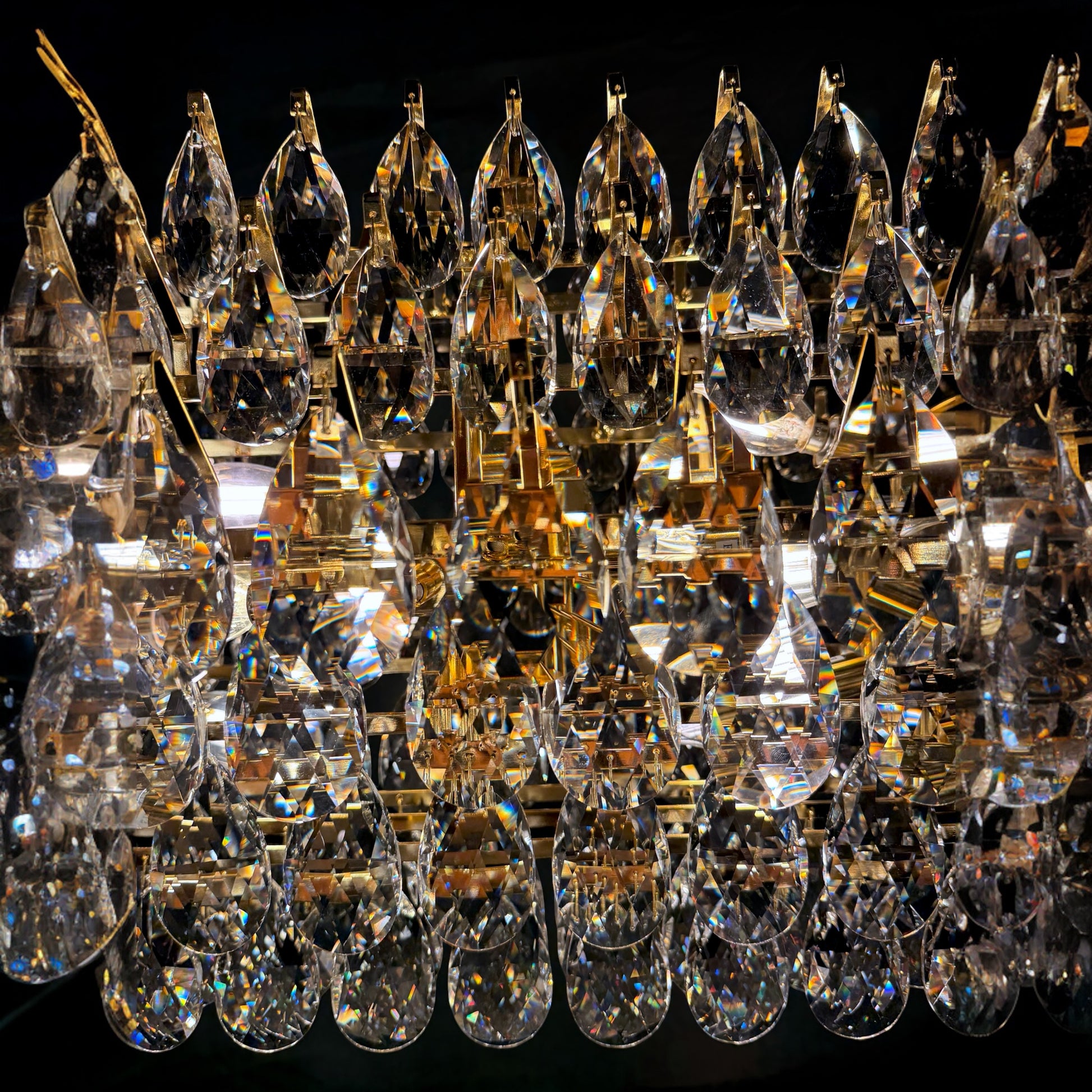 An extreme close-up of premium teardrop crystals on a linear chandelier, showcasing their clarity, facets, and maximum sparkle against a dark backdrop.

