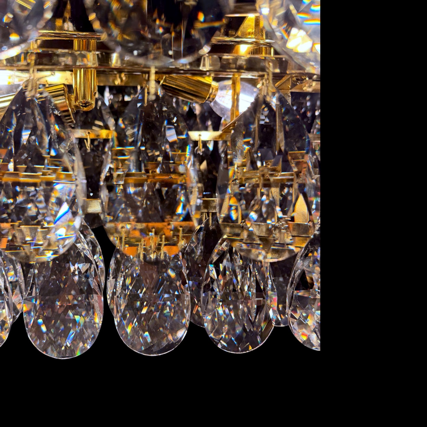 An extreme close-up of premium teardrop crystals on a linear chandelier, showcasing their clarity, facets, and maximum sparkle against a dark backdrop.
