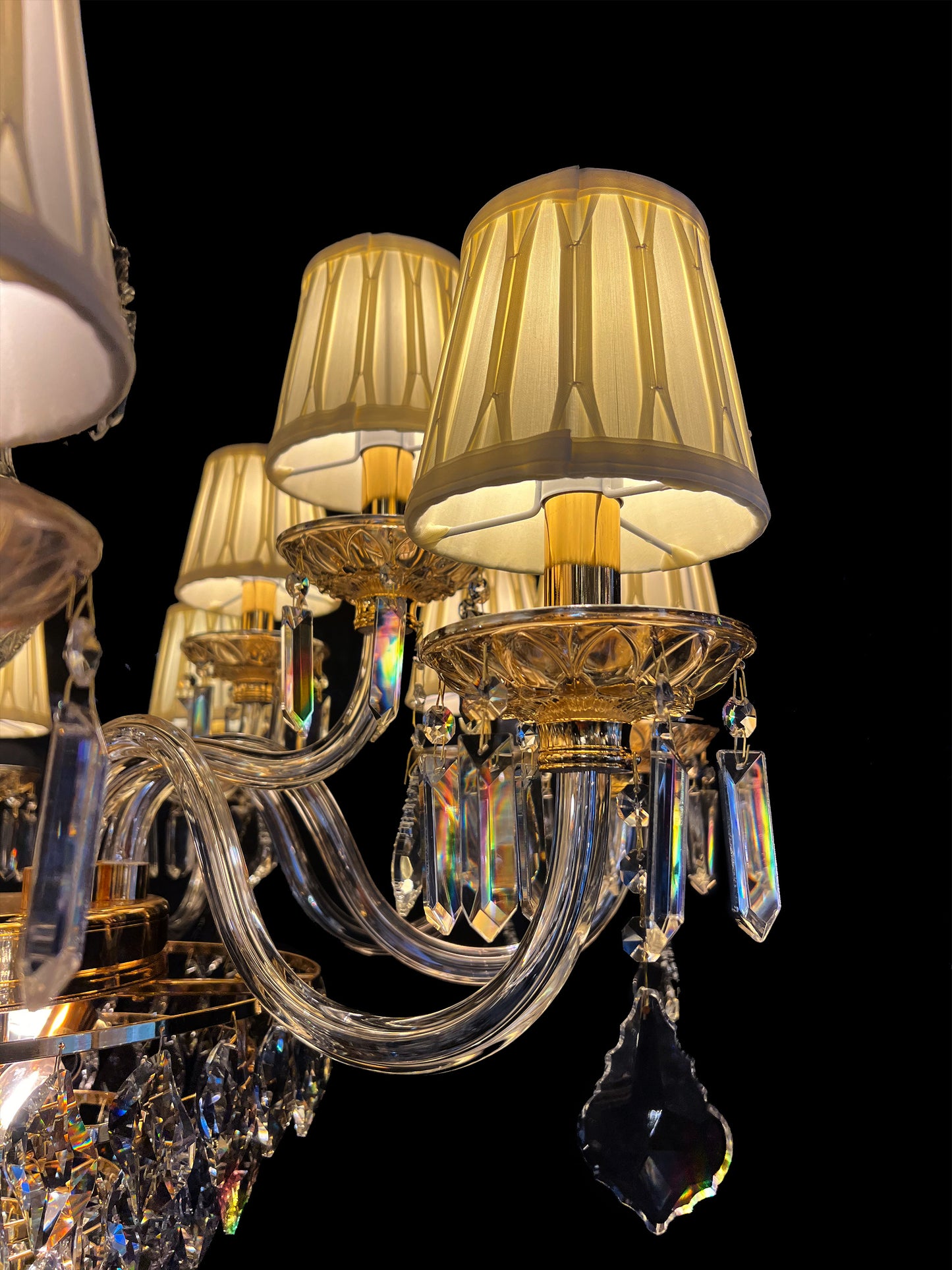 Detailed view of chandelier arm with pleated fabric shade and hanging crystal drops, highlighting the brilliance of gold finish and craftsmanship.