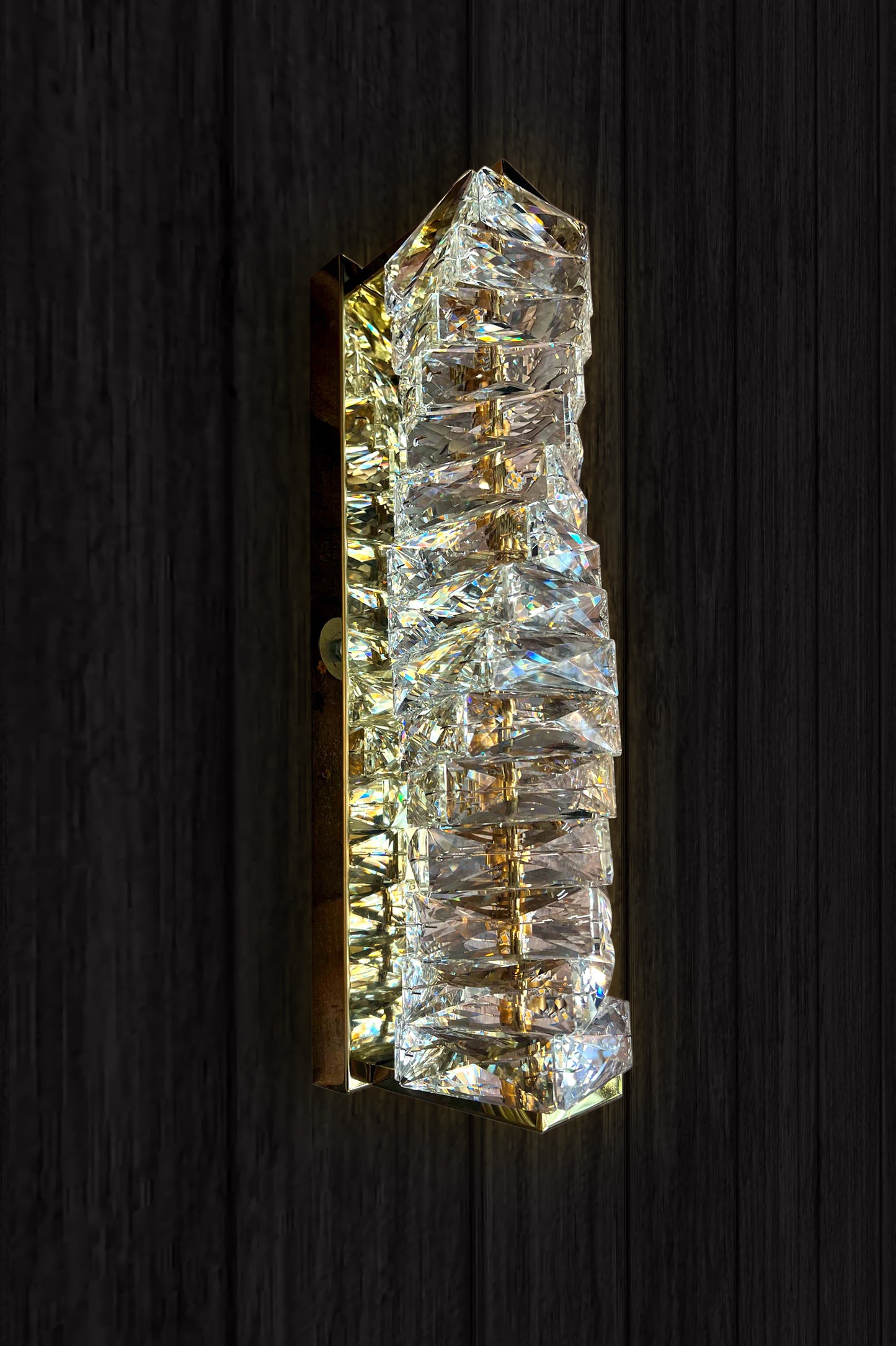 A luxury crystal wall lamp with a modern gold finish, featuring a vertical crystal shade and integrated LED light strip.