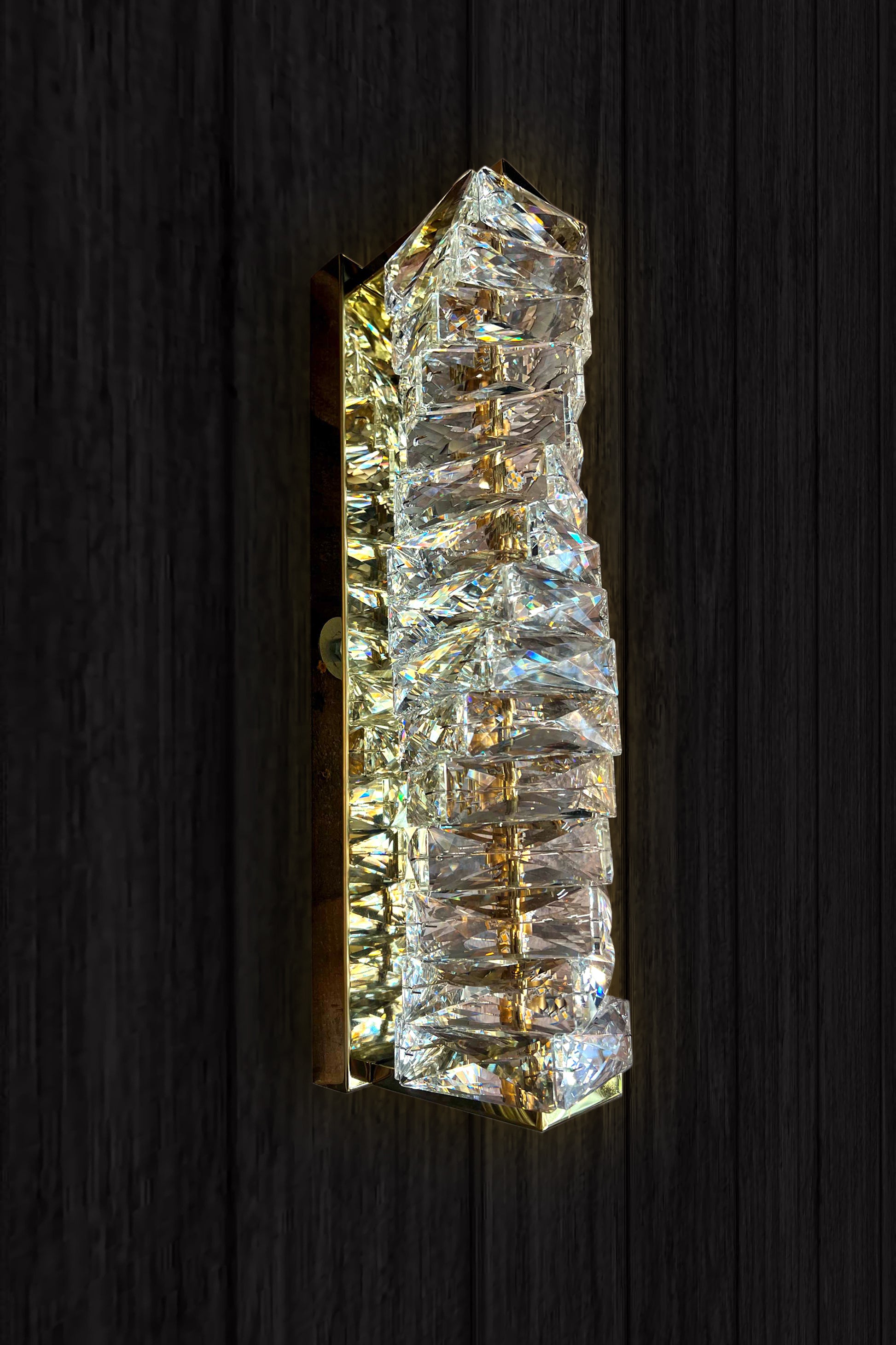 A luxury crystal wall lamp with a modern gold finish, featuring a vertical crystal shade and integrated LED light strip.