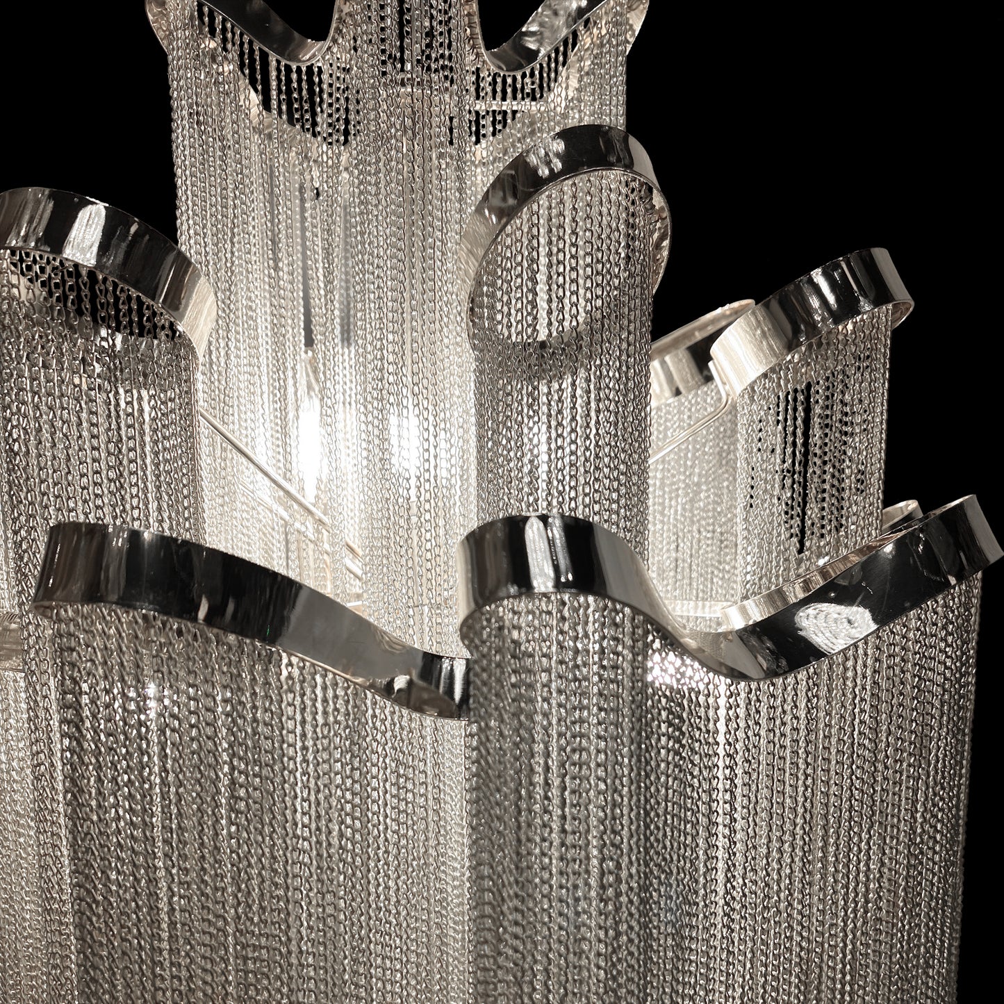 Detailed macro shot highlighting the stainless steel frame and reflective chrome chains of the chandelier’s upper tier.
