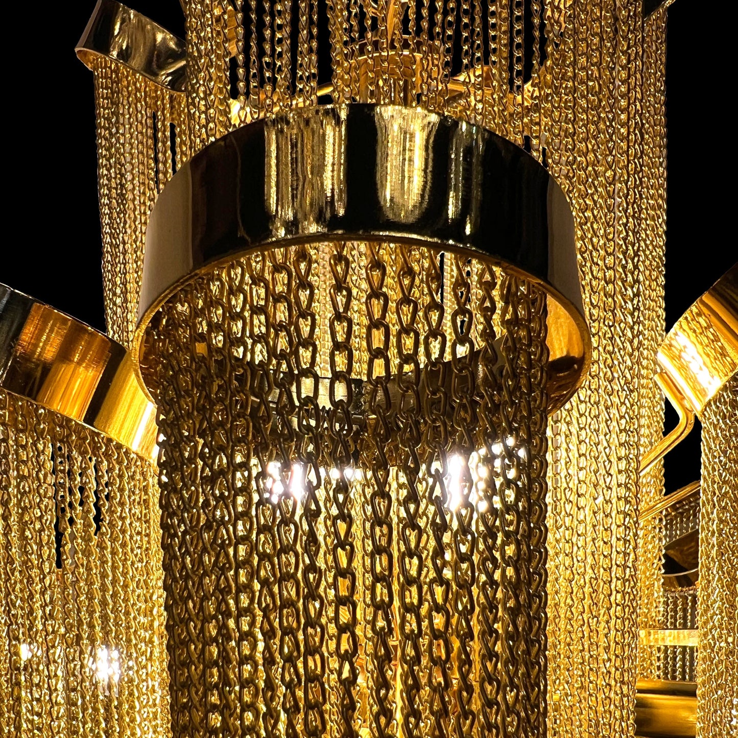Detailed macro shot highlighting the stainless steel frame and reflective gold chains of the chandelier’s upper tier.
