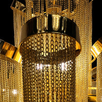 Detailed macro shot highlighting the stainless steel frame and reflective gold chains of the chandelier’s upper tier.
