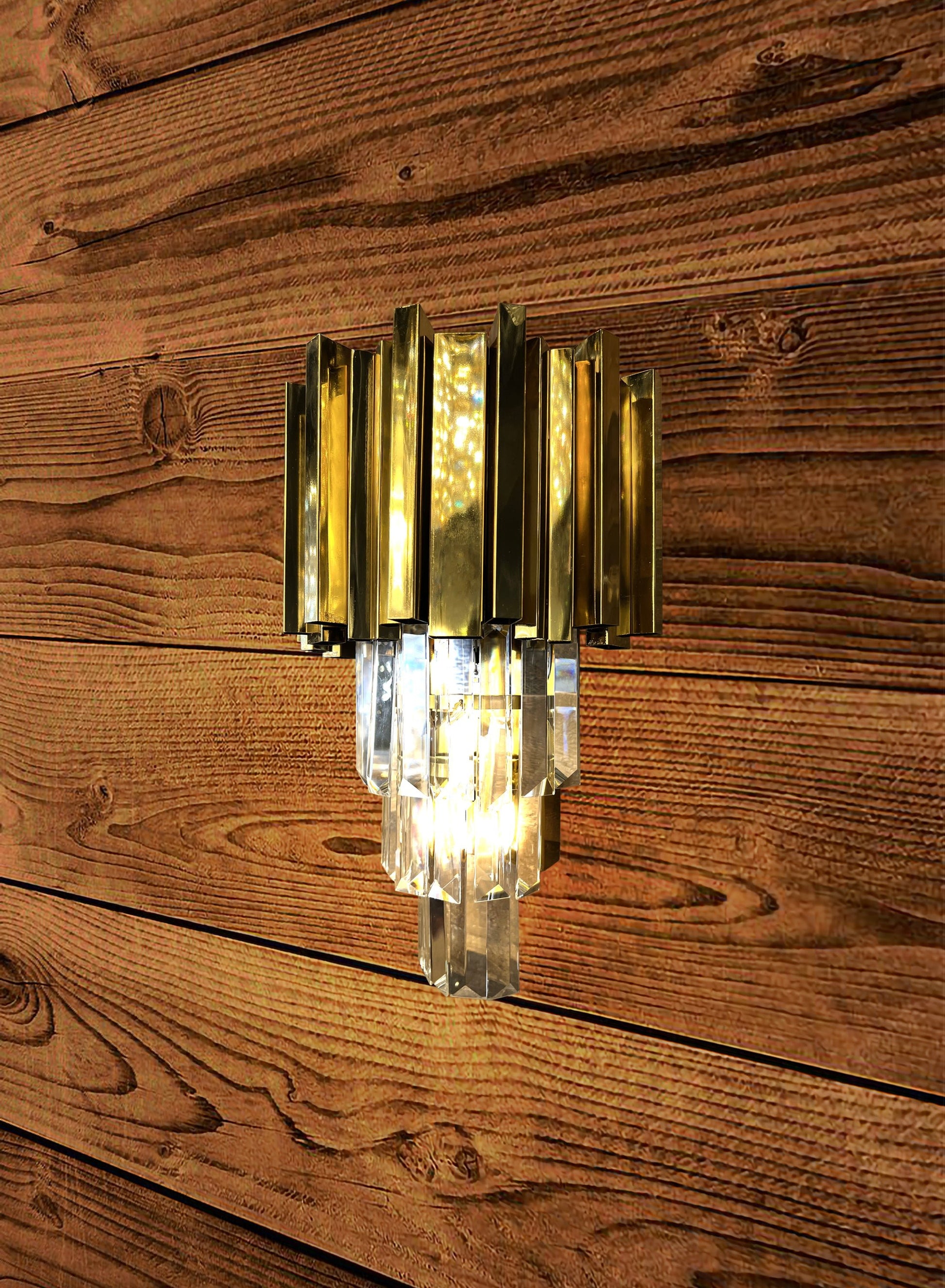 Wall-mounted light fixture with gold and clear design on a wooden wall.