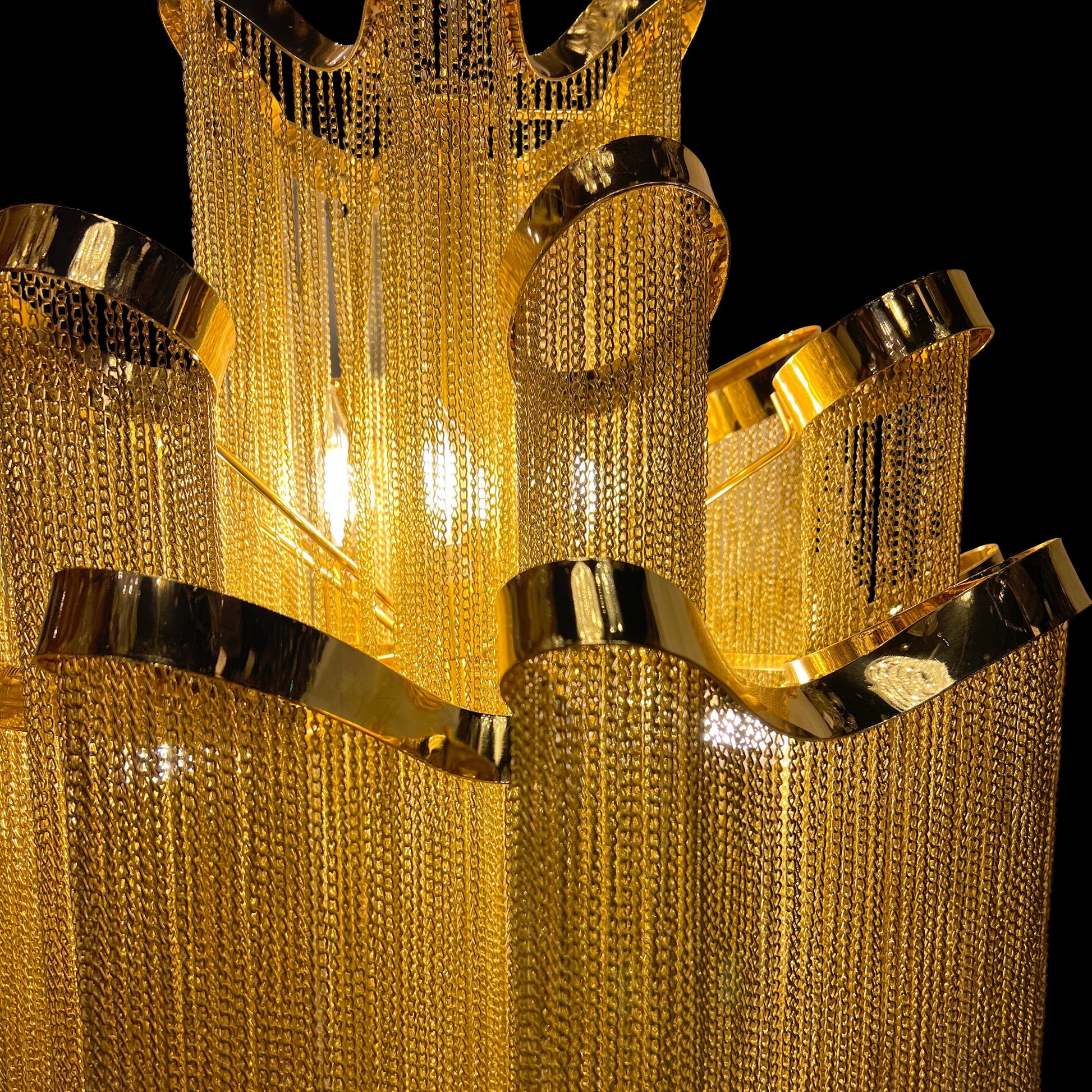 Detailed macro shot highlighting the stainless steel frame and reflective gold chains of the chandelier’s upper tier.
