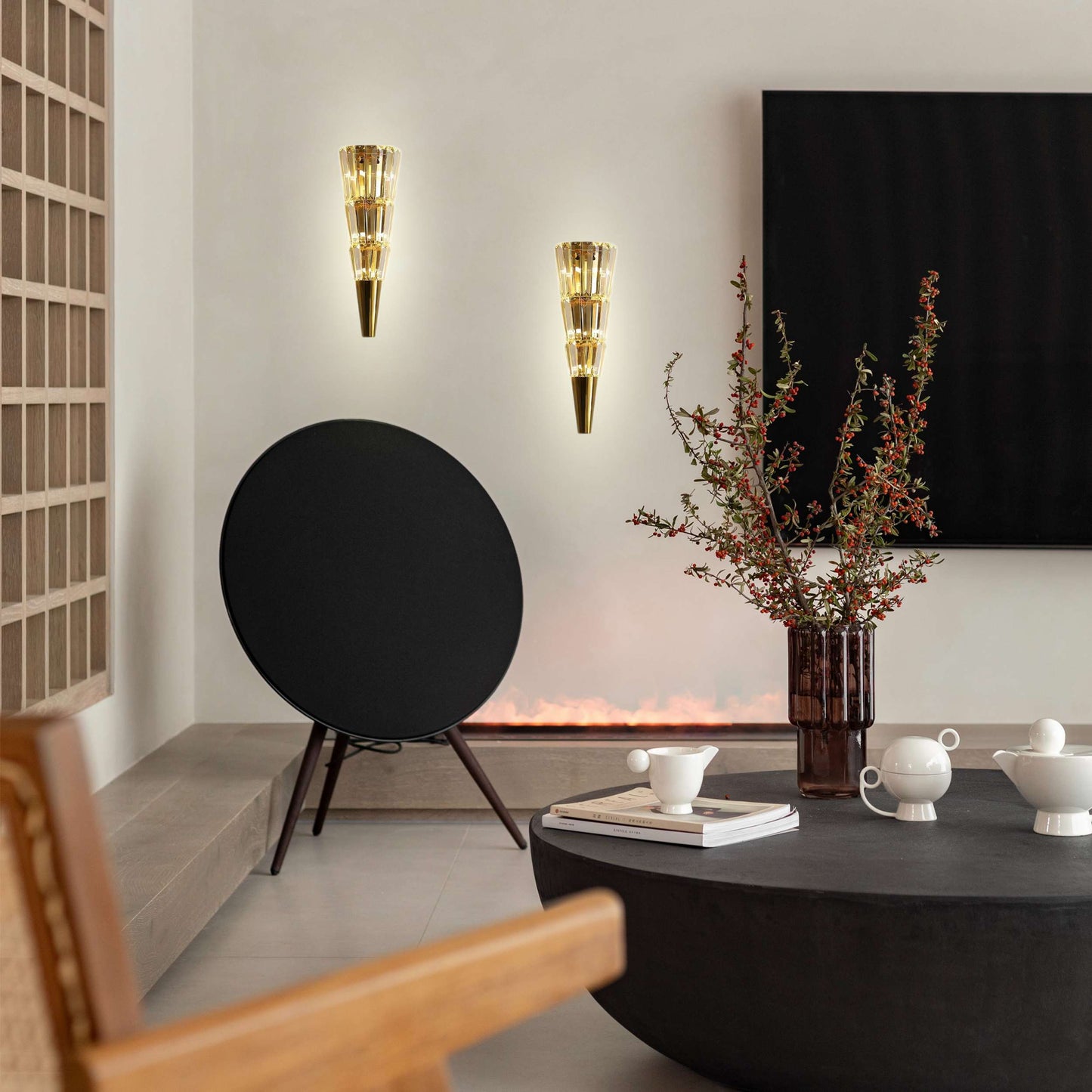 Modern living room with a black round speaker, wall sconces, and a vase with branches.