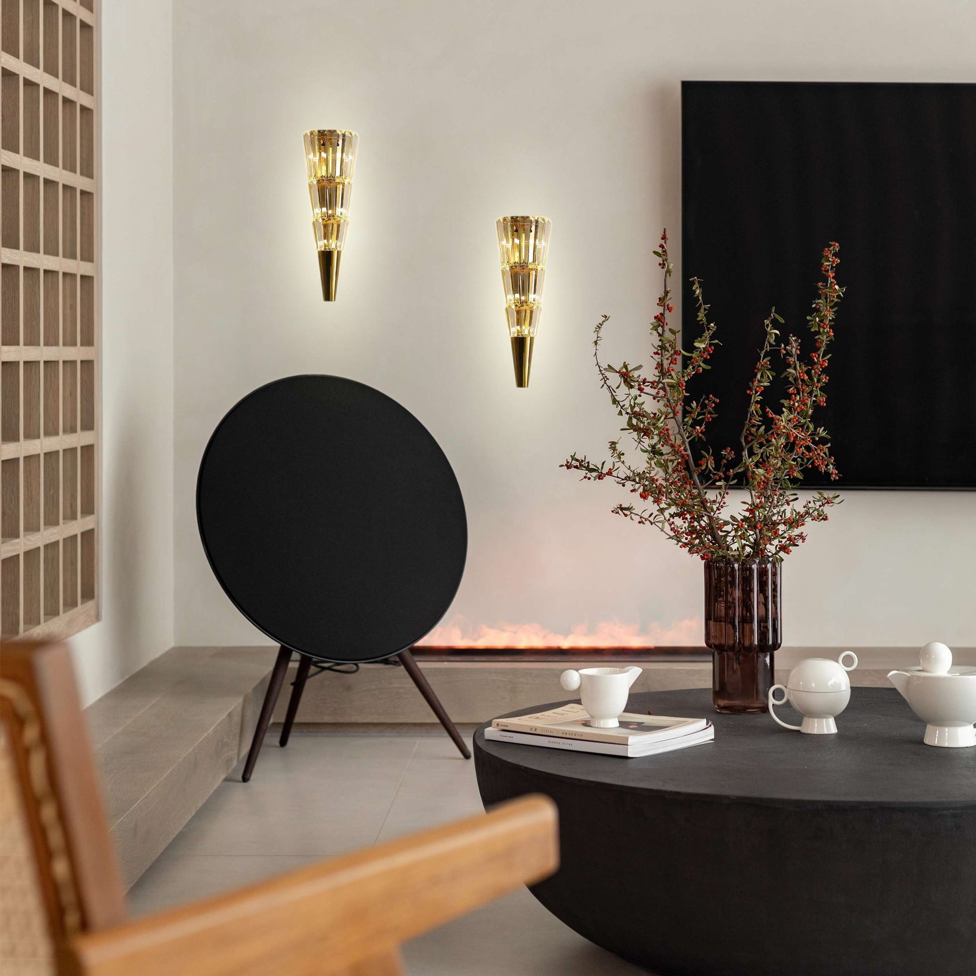 Modern living room with a black round speaker, wall sconces, and a vase with branches.