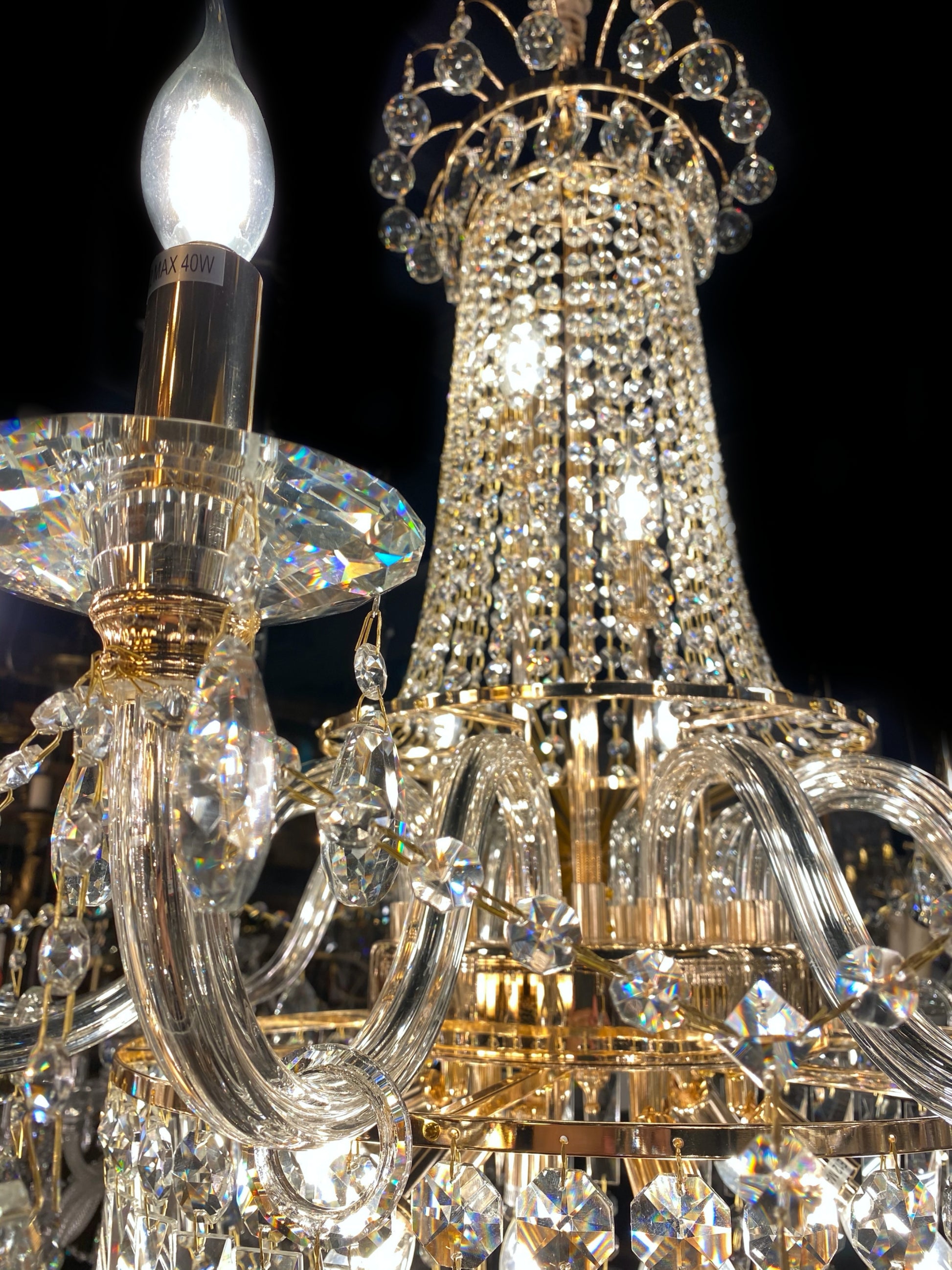Upper section of chandelier featuring curved gold arms and crystal chains.”