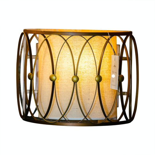 A modern bronze wall sconce with an oval cage design and a linen fabric shade, viewed from a slightly elevated angle.
