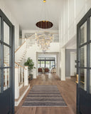 Dimmable gold LED chandelier with adjustable hanging cables lighting up a tall entryway with staircase and high ceiling.