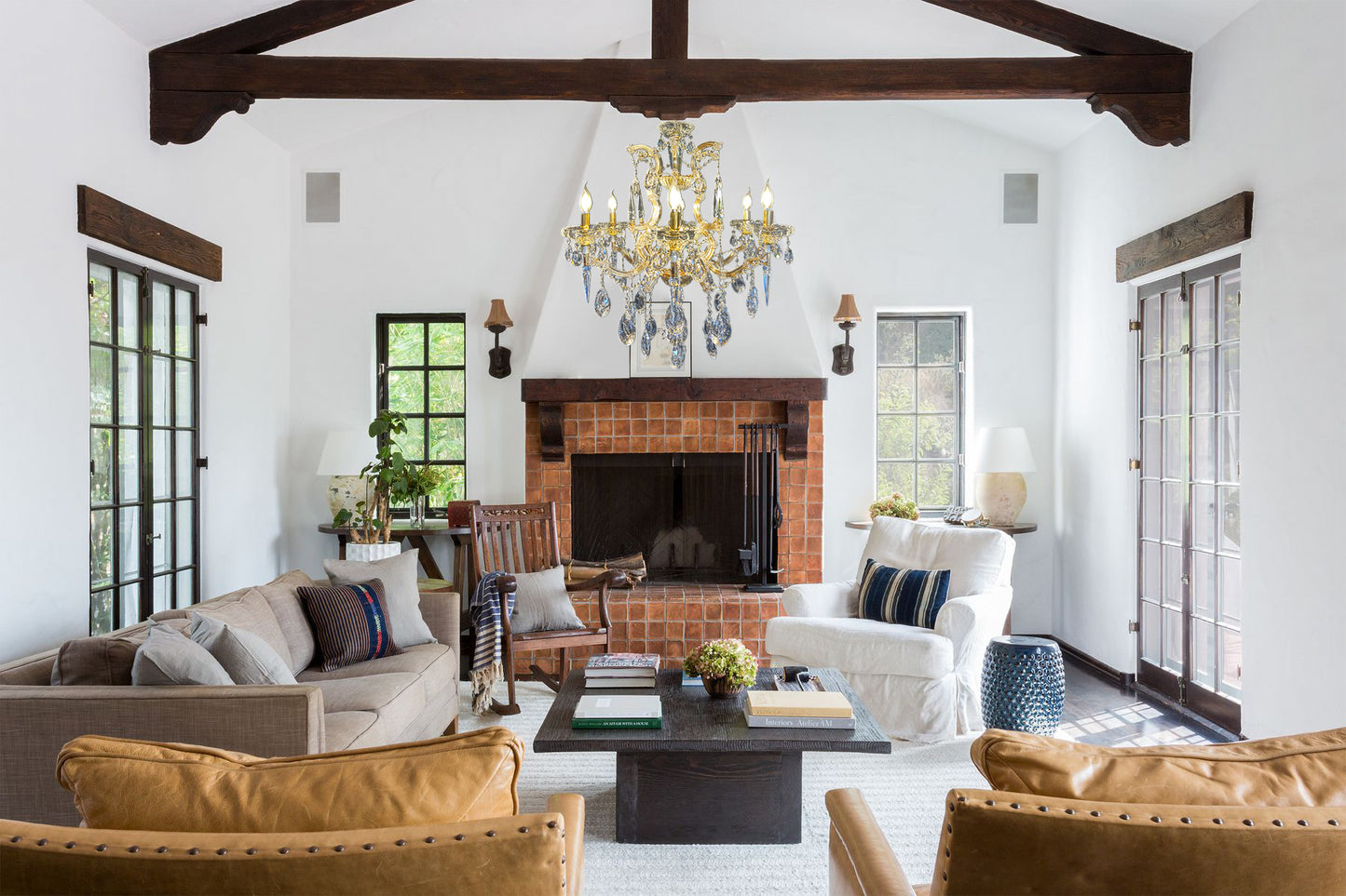 A luxurious living room with a gold-finished Maria Theresa crystal chandelier hanging from the ceiling, complemented by a fireplace and elegant furniture.